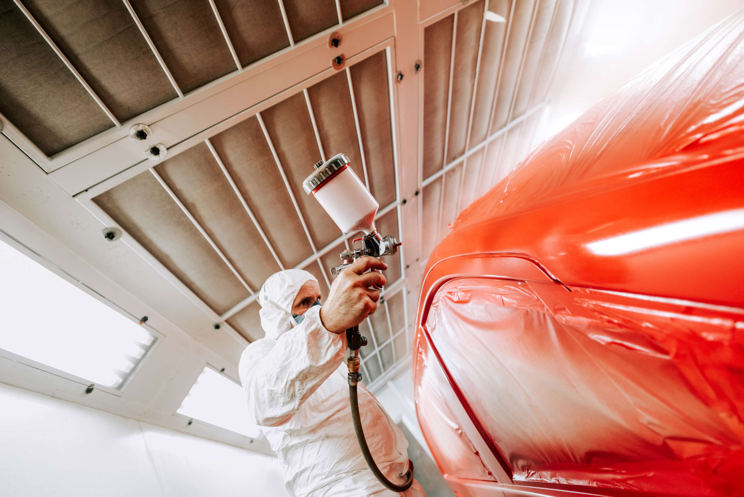 Automotive industry - auto engineer painting and working on a red body of car